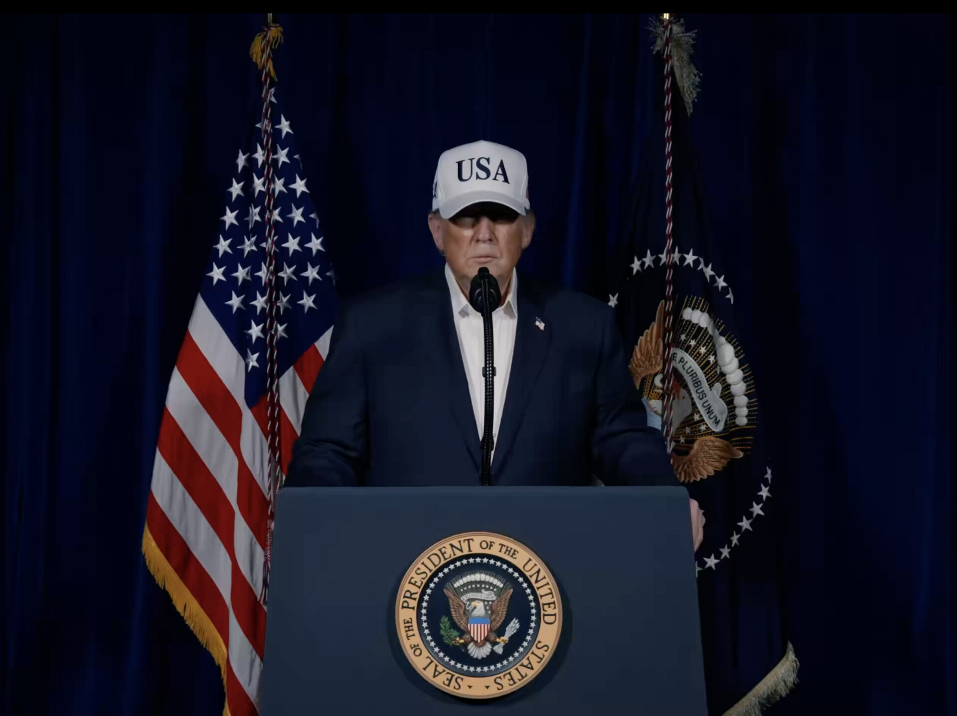 President Trump at a presidential podium announcing military action against Iran, February 28 2026, with US and presidential flags flanking him