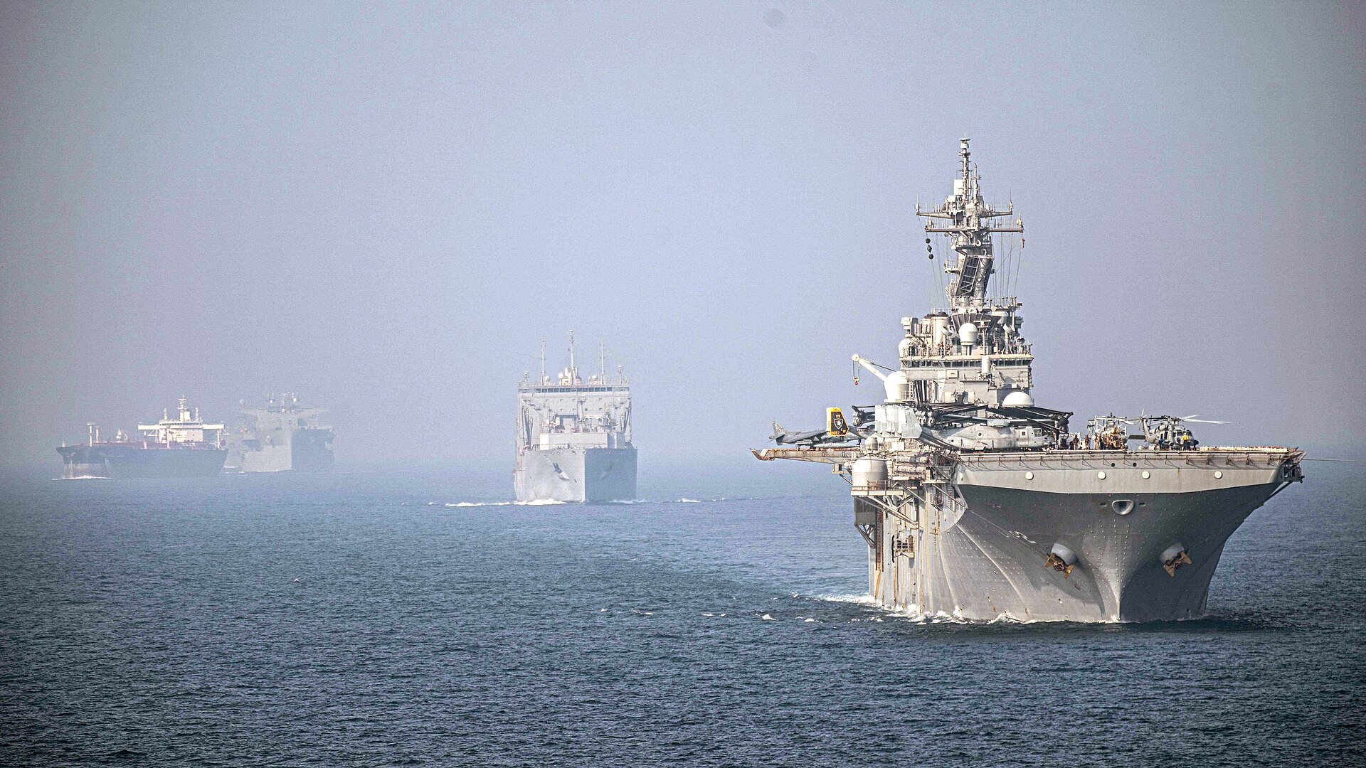 USS Essex (LHD-2) and USNS Wally Schirra (T-AKE 8) transit the Strait of Hormuz in formation, September 17, 2021. A civilian oil tanker is visible in the far background on the same shipping lane now subject to PGSA pre-clearance requirements. Photo: U.S. Navy / Public Domain