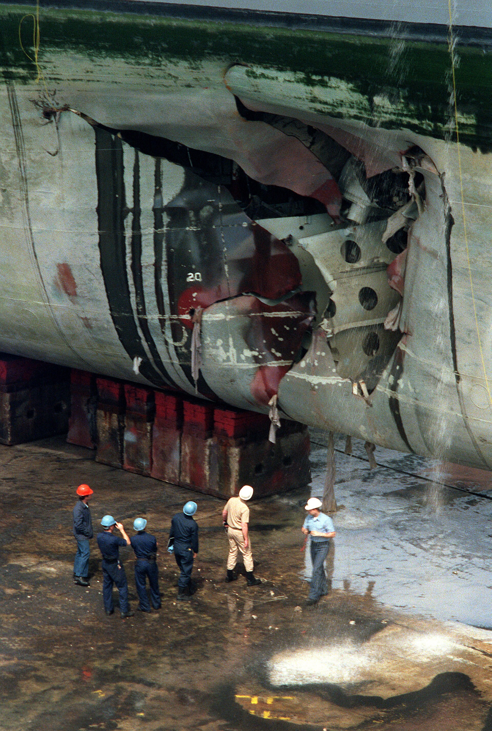 Repair crews inspect the mine-damaged hull of USS Tripoli (LPH-10) in dry dock after the ship struck an Iraqi mine in the northern Persian Gulf on February 18, 1991