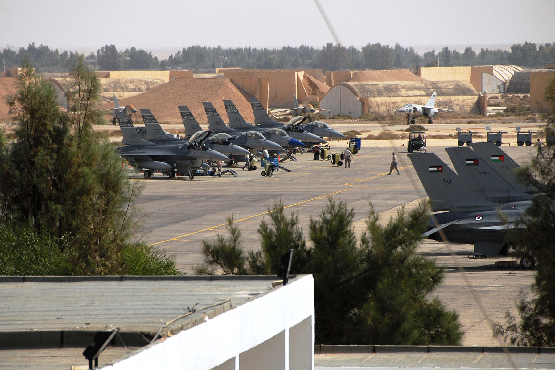 F-16 Fighting Falcons on the apron at Muwaffaq Salti Air Base near Azraq, Jordan, with Royal Jordanian Air Force markings visible on the tails and hardened aircraft shelters behind