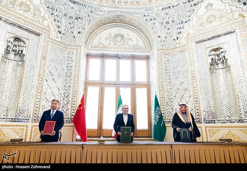 Iranian, Saudi, and Chinese officials at the China-Saudi Arabia-Iran joint trilateral committee session in an ornate Iranian diplomatic hall, all three sides holding documents with national flags displayed
