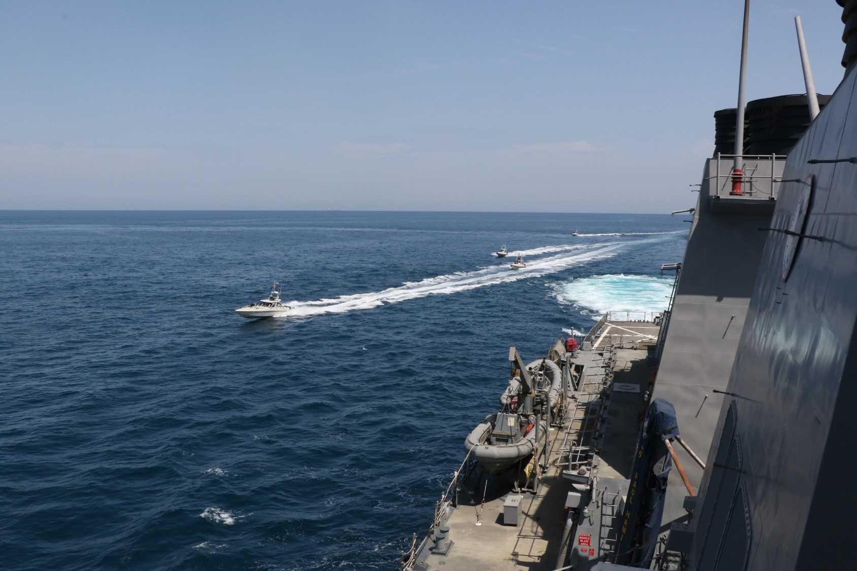 IRGC Navy fast attack speedboats cross the bow of guided-missile destroyer USS Paul Hamilton in the Persian Gulf — the same harassment pattern that Raja News cited as proof of IRGC Hormuz control independent of any MOU