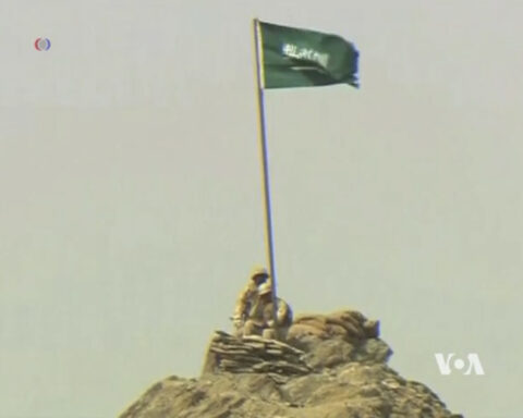 Saudi coalition soldier plants flag on rocky mountain peak in Yemen, 2015, reflecting the elevated terrain combat zones of the Hodeidah front