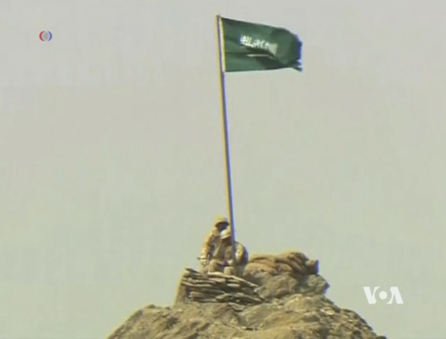 Saudi coalition soldier plants flag on rocky mountain peak in Yemen, 2015, reflecting the elevated terrain combat zones of the Hodeidah front
