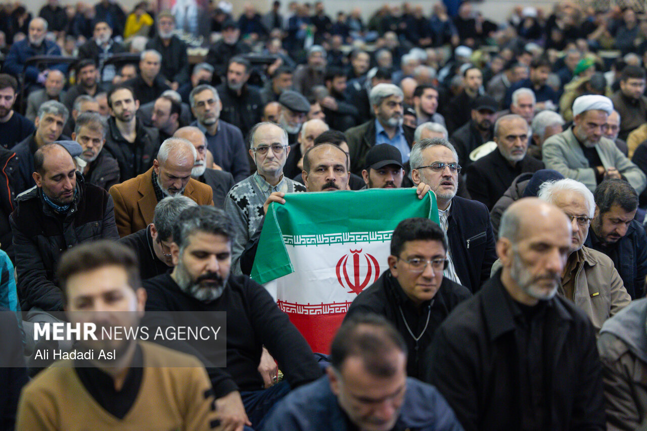 Iranian mourners inside Tehran Grand Mosalla, one holding an Iranian flag, during a state ceremony at the IRGC-managed venue