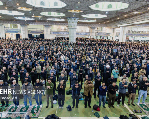 Interior of Imam Khomeini Grand Mosalla in Tehran filled with thousands of worshippers during a major state ceremony, showing the iconic octagonal dome and marble columns