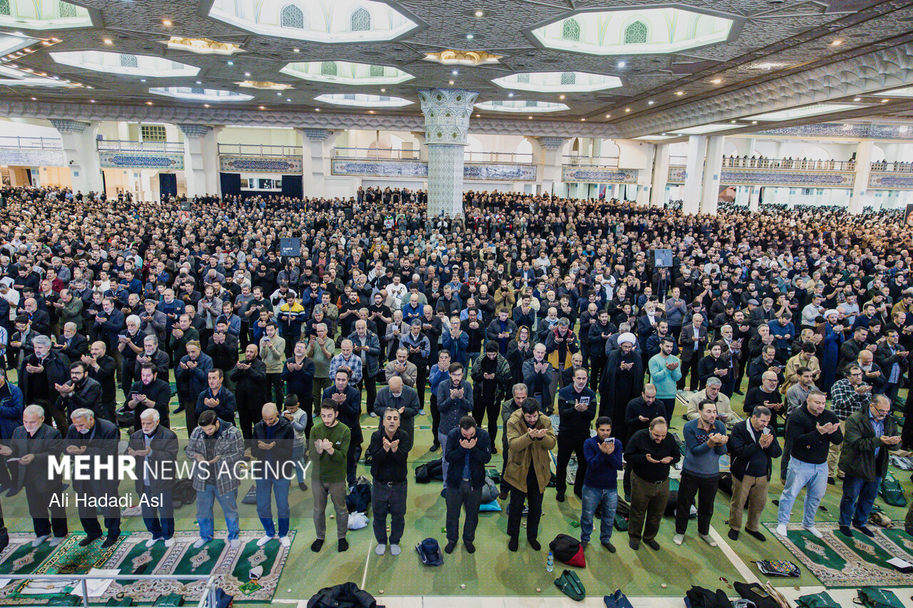 Interior of Imam Khomeini Grand Mosalla in Tehran filled with thousands of worshippers during a major state ceremony, showing the iconic octagonal dome and marble columns