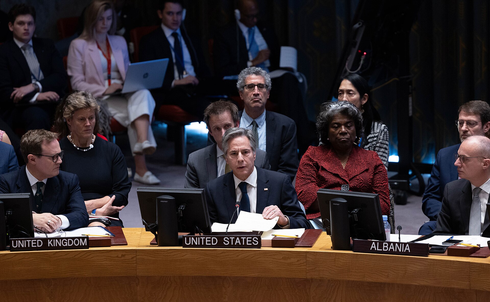 The UN Security Council horseshoe table during a Middle East ministerial session, showing the UNITED STATES, UNITED KINGDOM, and ALBANIA nameplates with delegates addressing the chamber