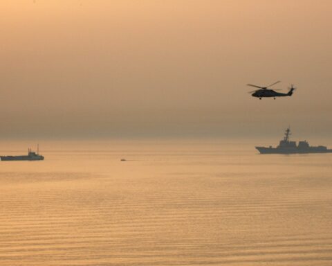 US Navy USS Mustin destroyer conducts Maritime Interdiction Operations in the Persian Gulf with helicopter overhead and vessel being intercepted