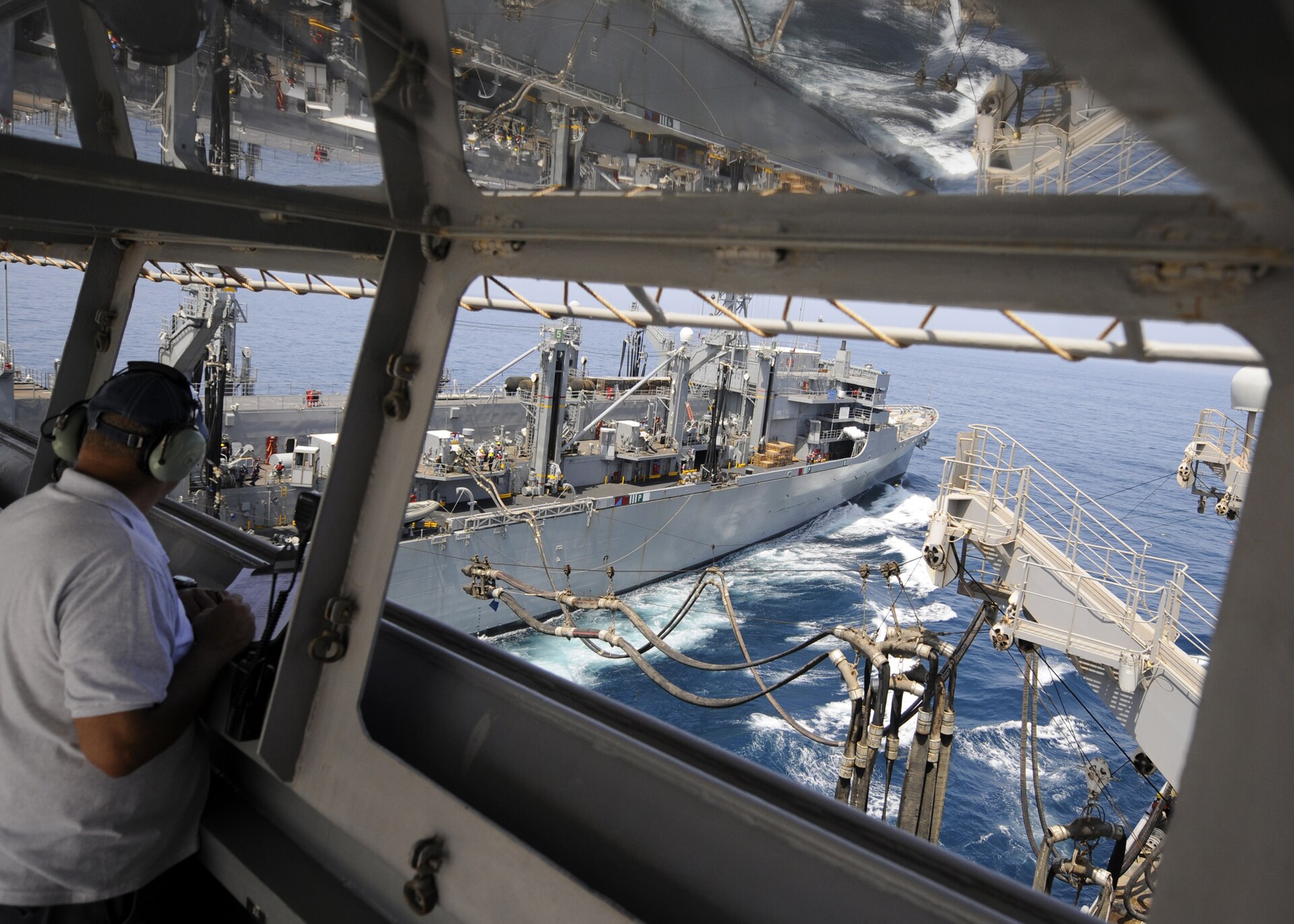 A civilian mariner aboard USNS Patuxent (T-AO 201) watches a fuel line being sent to USNS Supply during naval replenishment at sea in the Gulf of Oman, April 2012