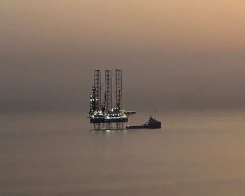 A Saudi Aramco offshore oil rig lit against a hazy Gulf sunset, with a supply vessel moored alongside — the Eastern Province holds the world's largest proven oil reserves