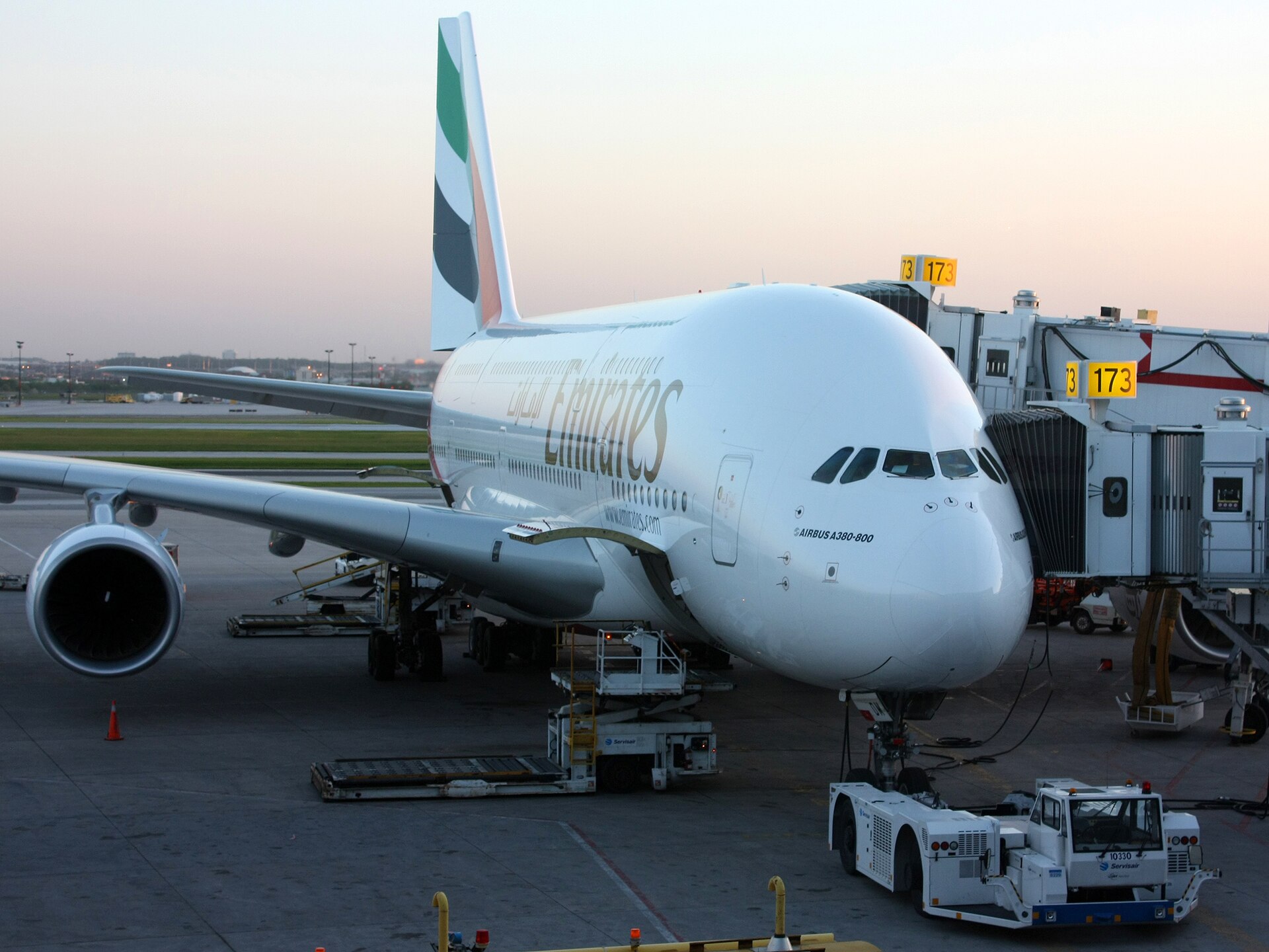 Emirates Airbus A380-800 parked at an airport gate with jet bridges connected, photographed at dusk