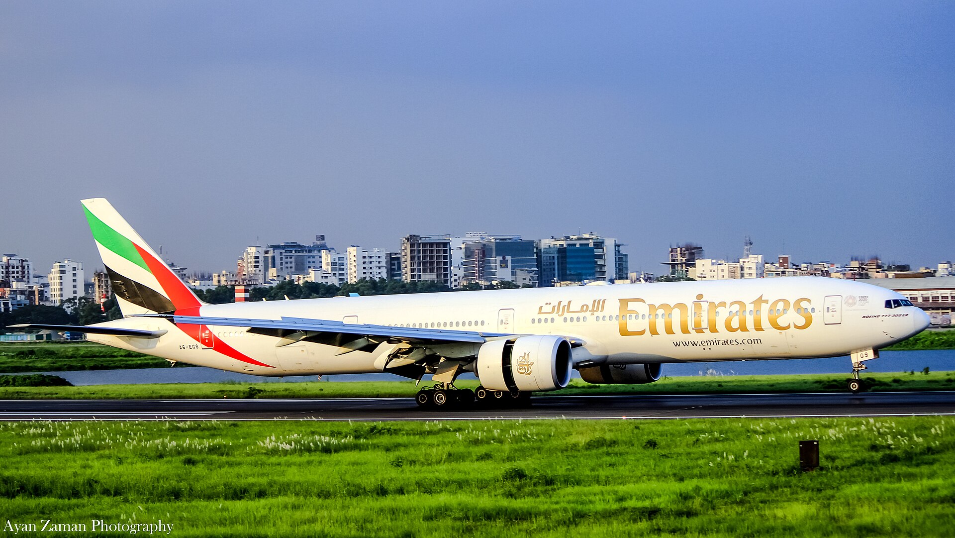 Emirates Boeing 777-300ER on runway, with Emirates livery and gold script markings visible on fuselage