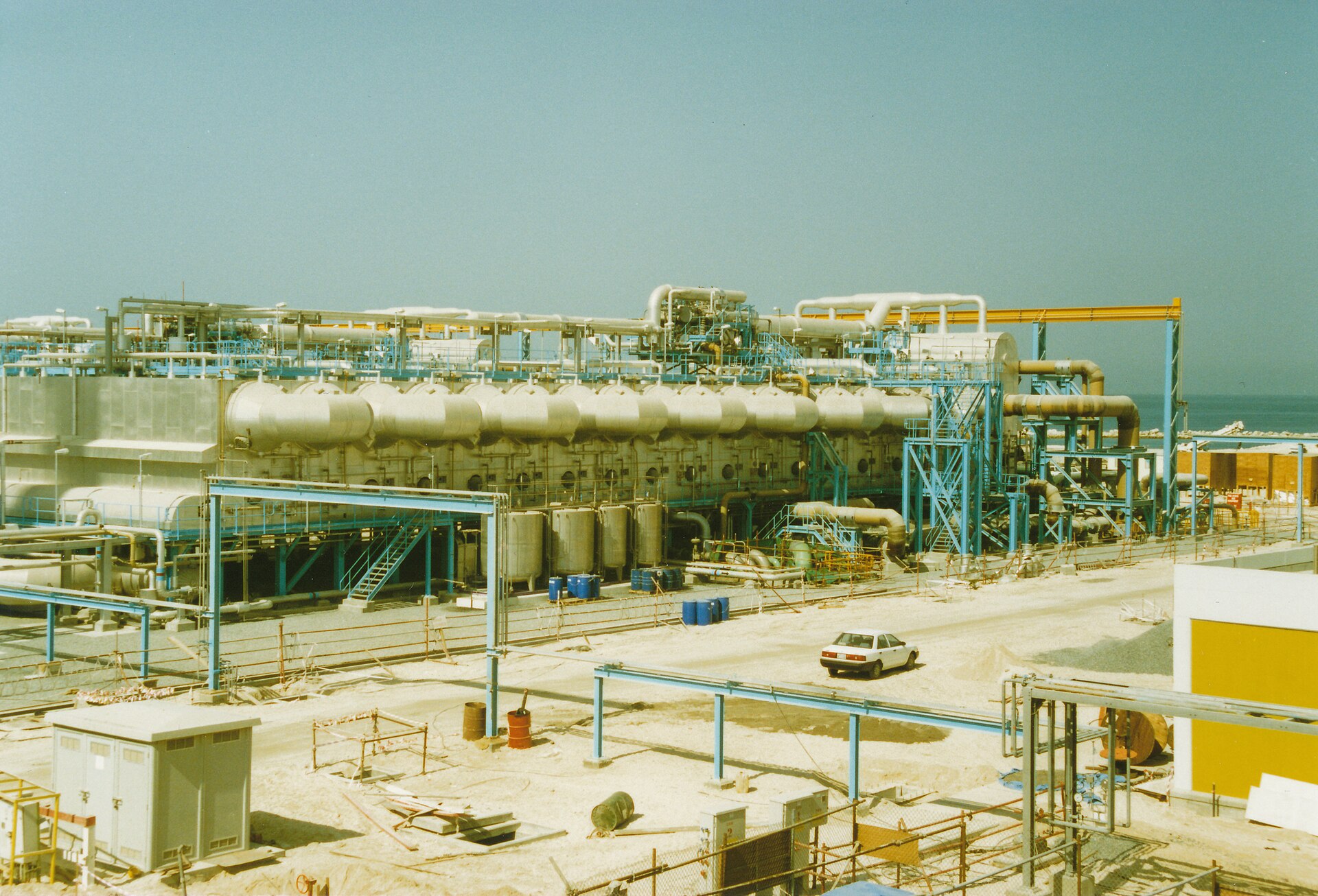 Multi-stage flash desalination plant at Jebel Ali G Station Dubai UAE showing exposed tanks piping and the Gulf coast in the background
