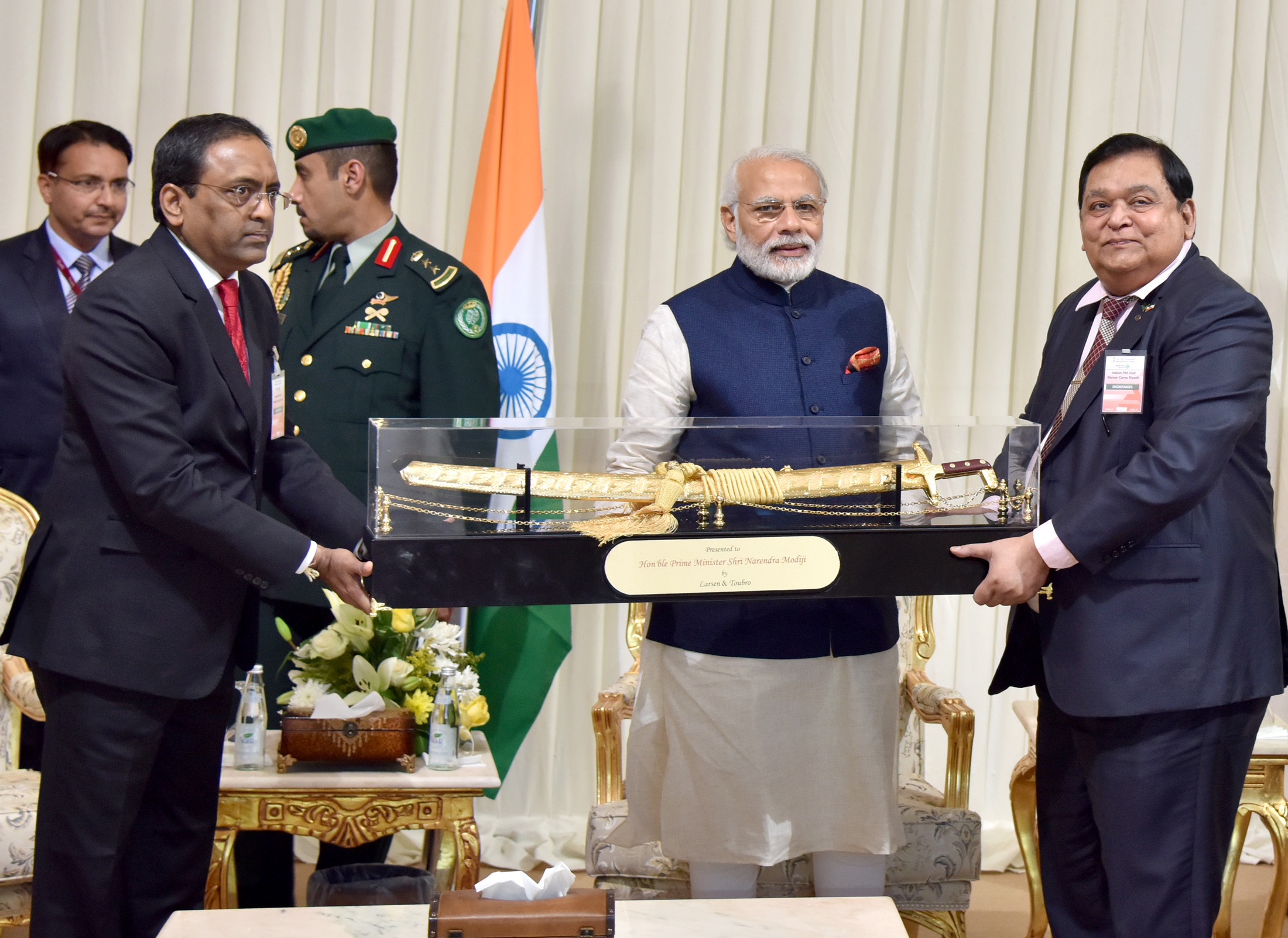 Prime Minister Narendra Modi receives a ceremonial memento from Larsen and Toubro executives at their Riyadh facility, with the Indian tricolour visible behind him, April 2016