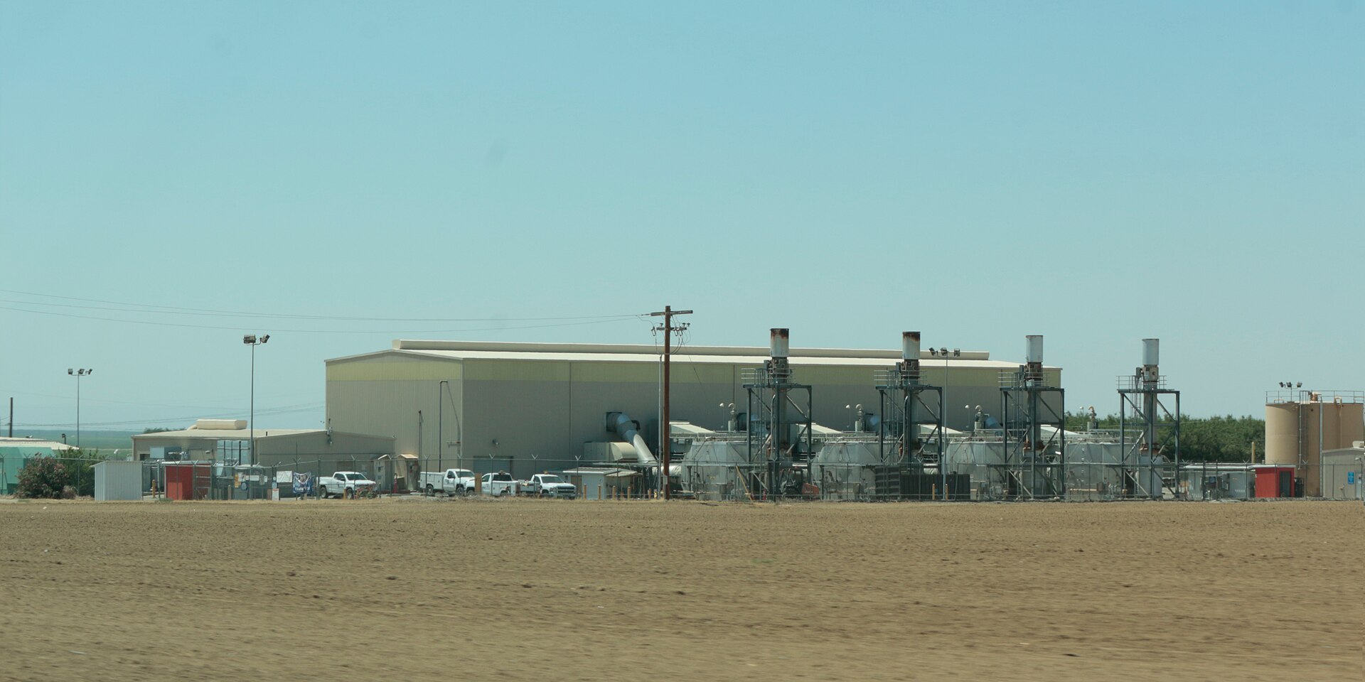 Oil pipeline compressor and pumping station in arid flat terrain showing industrial machinery, pipework, and pressure equipment