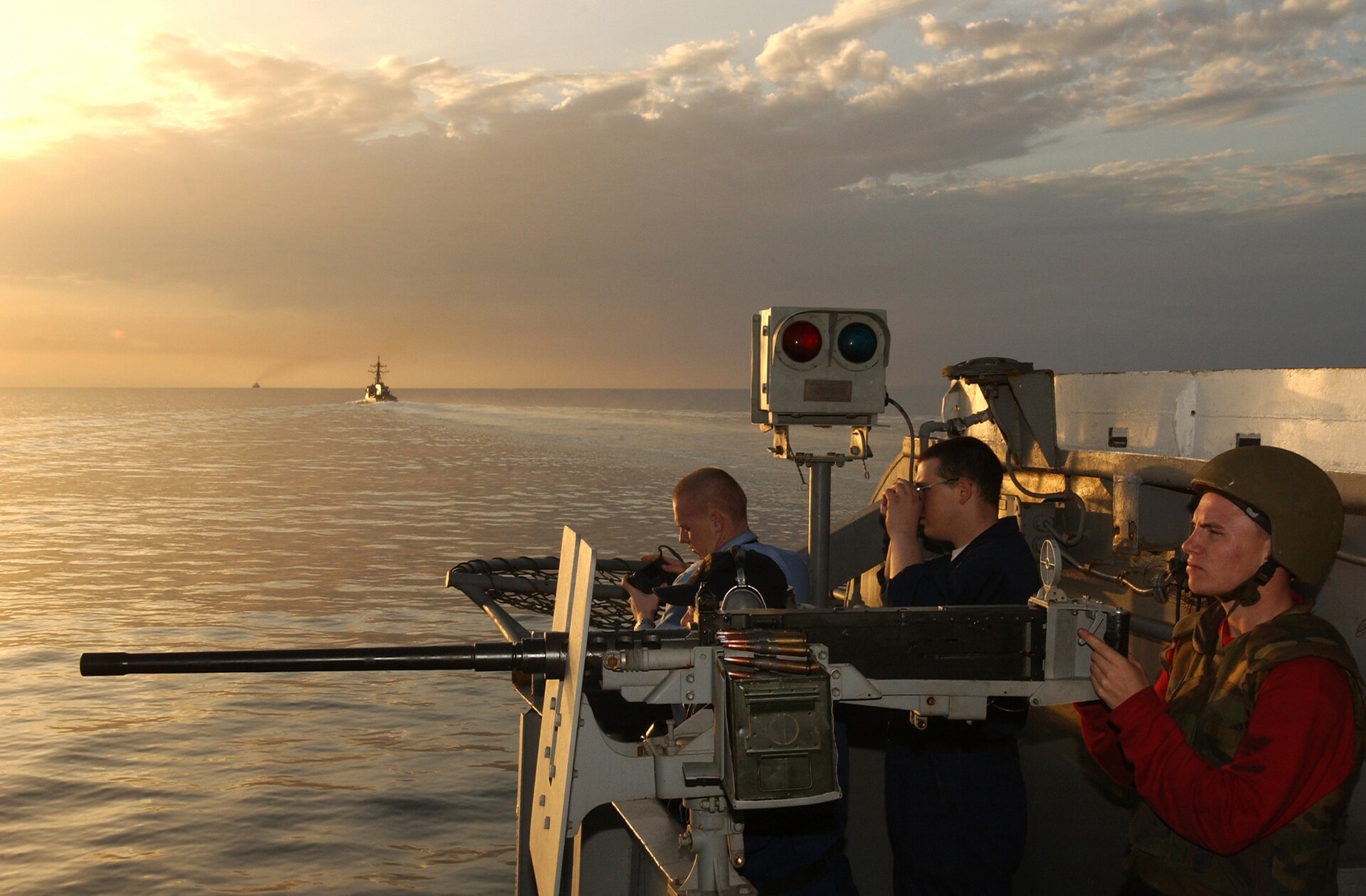 US Navy sailors man a .50-caliber machine gun on USS Kitty Hawk bow while transiting the Strait of Hormuz with escort destroyer in background
