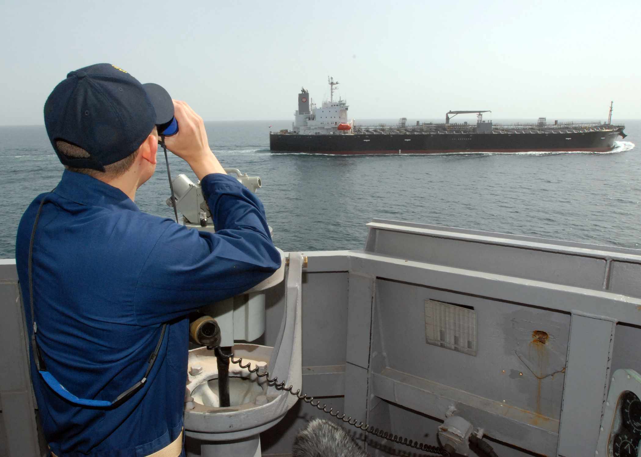 A US Navy officer aboard USS Paul Hamilton (DDG 60) tracks an oil tanker transiting the Persian Gulf through binoculars