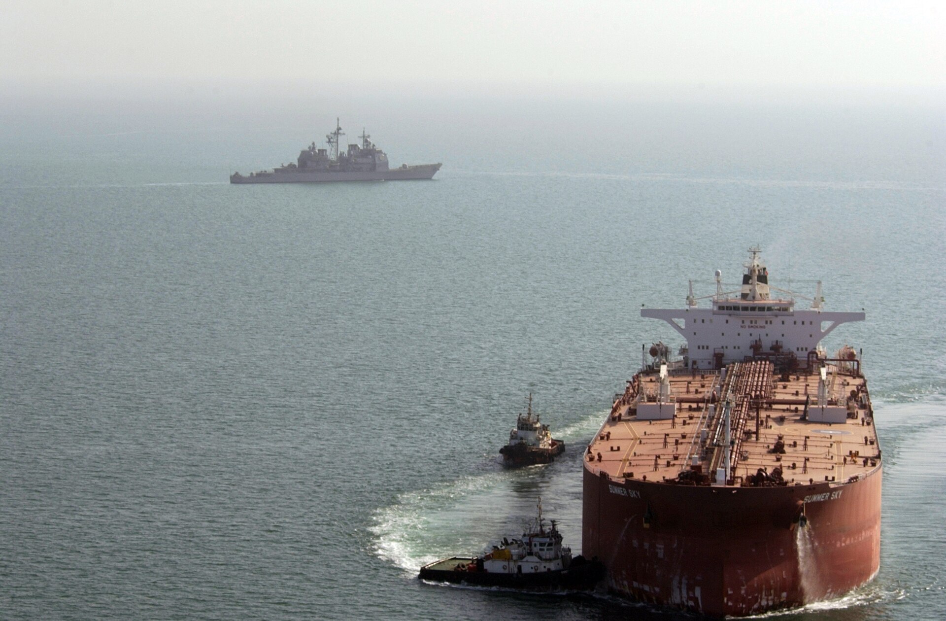 USS Mobile Bay (CG-53) guided missile cruiser patrols the Persian Gulf as the supertanker Summer Sky is guided into position at Iraq's Al Basrah Oil Terminal — the type of crude-oil loading infrastructure whose exports depend on open access through the Strait of Hormuz