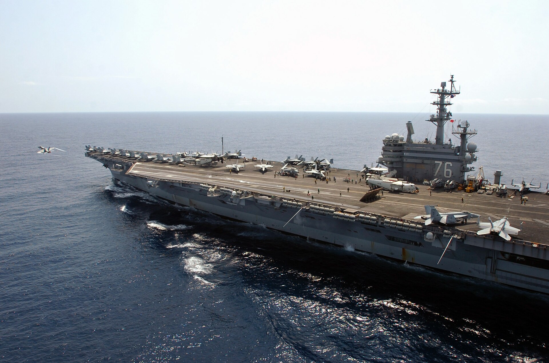 USS Ronald Reagan (CVN-76) with F/A-18 Hornet launching from flight deck — a Nimitz-class carrier strike group represents the US power projection that Washington has withheld from the Gulf in 2026